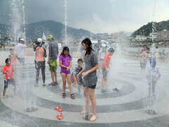 광장 바닥에서 분수처럼 물이 하늘을 향해 솟아오르고 어른들과 아이들이 물을 맞으면서 즐기고 있는 모습