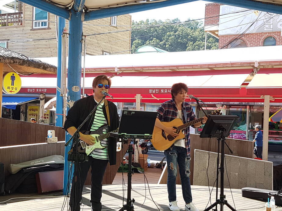 두명의 남성이 토요시장에서 기타를 치며 공연을 하고 있다.