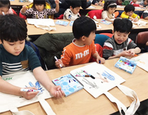 초등학생들이 책상에 앉아 에코백위에 색색의 사인펜으로 그림을 그리는 모습
