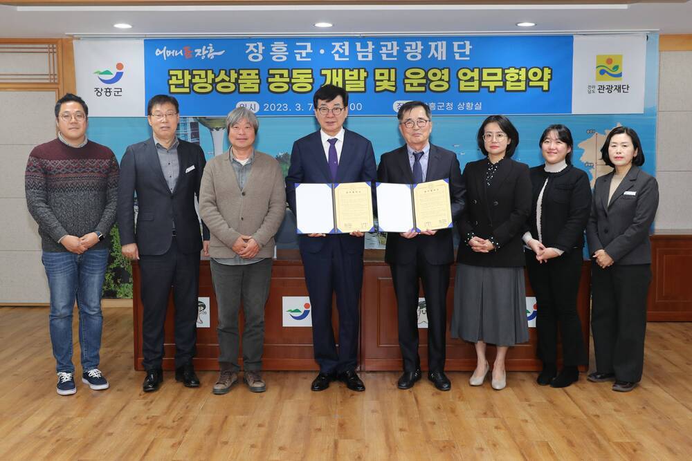 플래카드-장흥군·전남관광재단 관광상품 공동 대발 및 운영 업무협약 일시 2023.3.7(화) 14:00, 장소 장흥군청 상황실, 업무협약서를 들고 나란히 서있는 장흥군수와 전남관광재단 대표이사 및 관계자들 6인 단체 사진